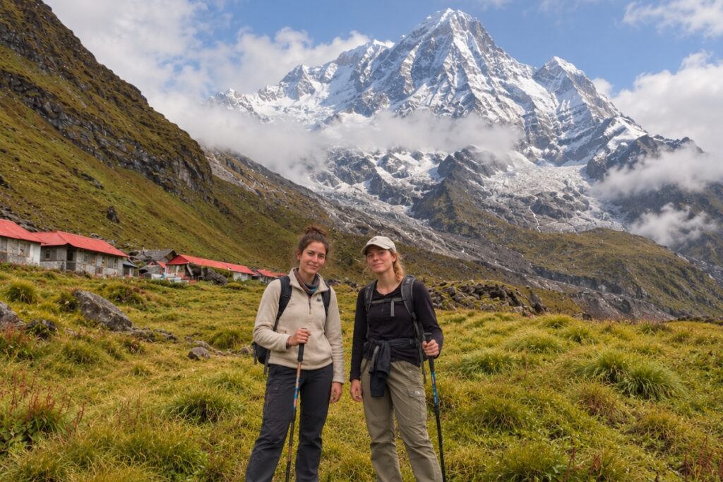 Two trekkers walking through the Annapurna Base Camp trail with snow-covered mountains behind them