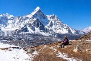 USA Solo Trekker – Everest Three Passes Trek USA solo trekker taking a break on the Everest Three Passes Trek with snow-covered Himalayan mountains