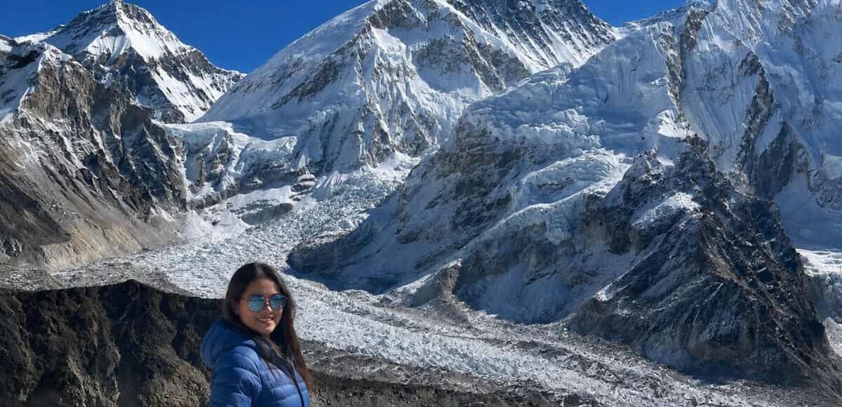 Trekker in a blue jacket on the Everest Base Camp trek, with the Khumbu Glacier and Mount Everest in the background