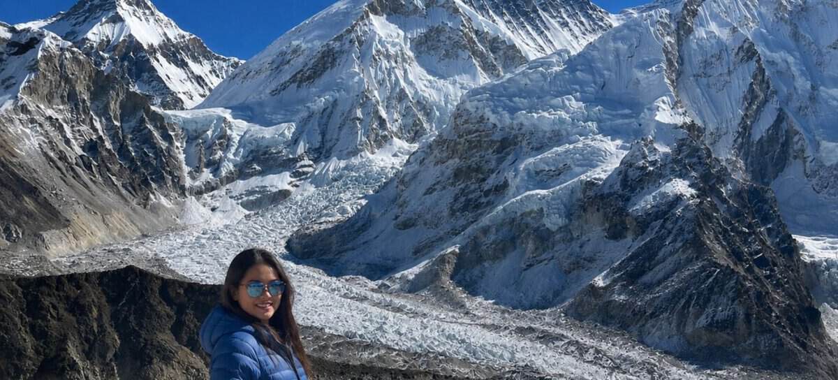 Trekker in a blue jacket on the Everest Base Camp trek, with the Khumbu Glacier and Mount Everest in the background
