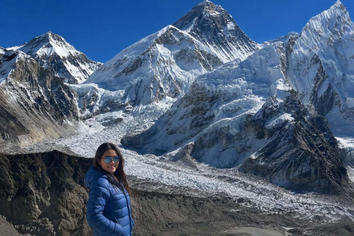 Trekker in a blue jacket on the Everest Base Camp trek, with the Khumbu Glacier and Mount Everest in the background