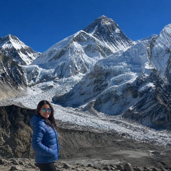 Trekker in a blue jacket on the Everest Base Camp trek, with the Khumbu Glacier and Mount Everest in the background