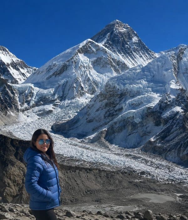 Trekker in a blue jacket on the Everest Base Camp trek, with the Khumbu Glacier and Mount Everest in the background