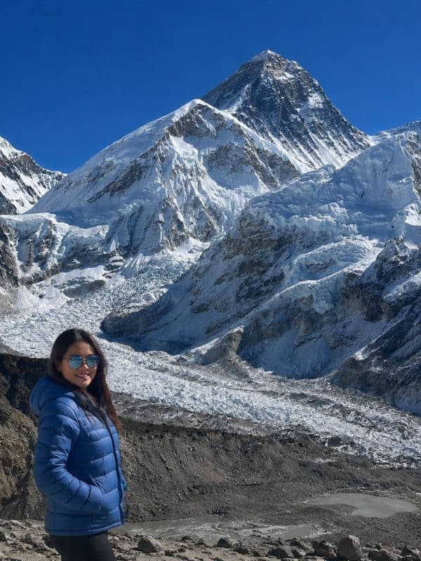 Trekker in a blue jacket on the Everest Base Camp trek, with the Khumbu Glacier and Mount Everest in the background