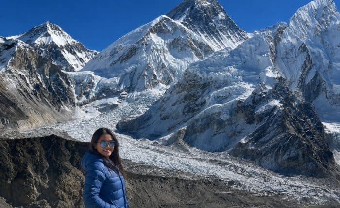 Trekker in a blue jacket on the Everest Base Camp trek, with the Khumbu Glacier and Mount Everest in the background