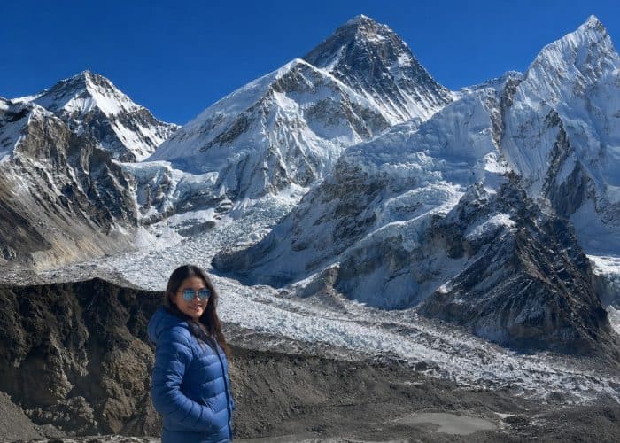Trekker in a blue jacket on the Everest Base Camp trek, with the Khumbu Glacier and Mount Everest in the background
