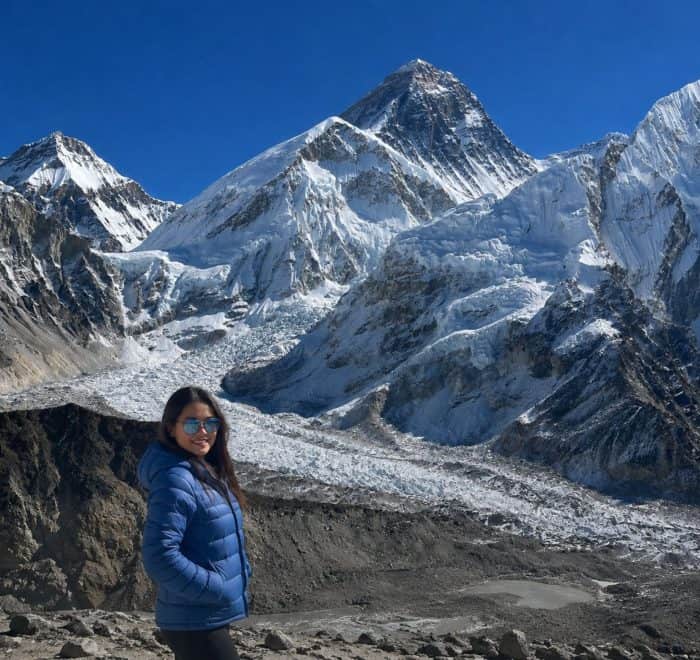 Trekker in a blue jacket on the Everest Base Camp trek, with the Khumbu Glacier and Mount Everest in the background