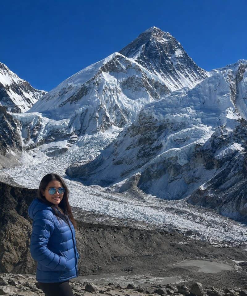 Trekker in a blue jacket on the Everest Base Camp trek, with the Khumbu Glacier and Mount Everest in the background
