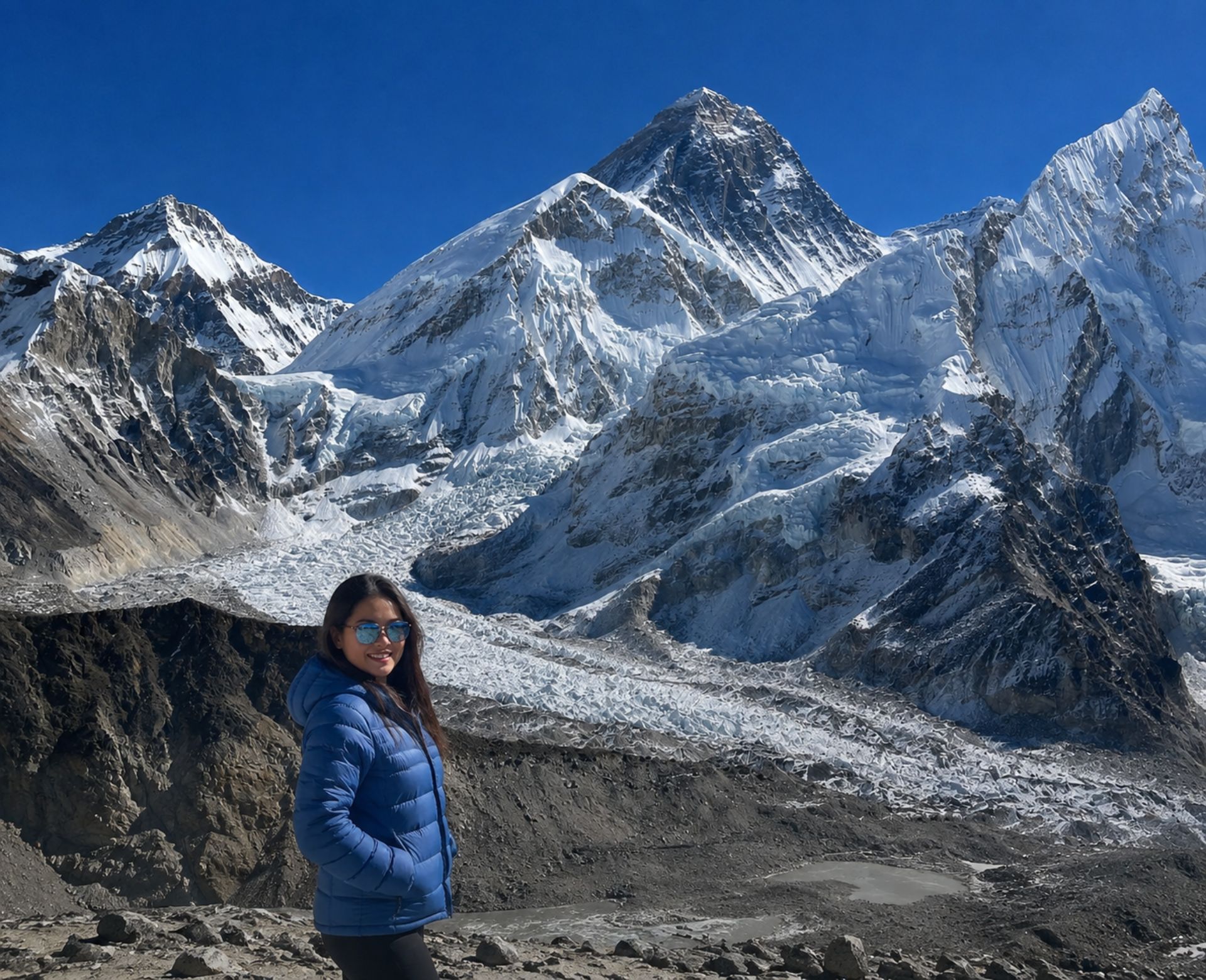 Trekker in a blue jacket on the Everest Base Camp trek, with the Khumbu Glacier and Mount Everest in the background