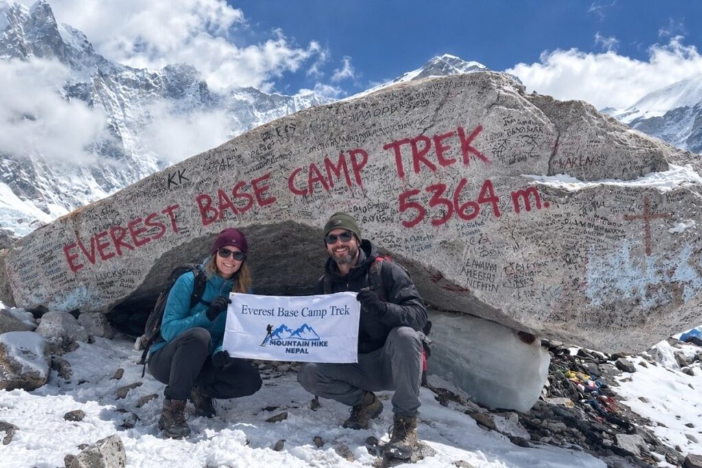 Two trekkers at Everest Base Camp with the 5,364-meter sign and snowy mountains
