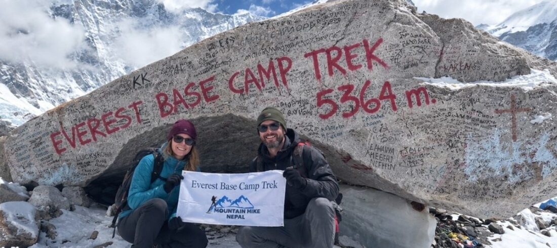 Two trekkers at Everest Base Camp with the 5,364-meter sign and snowy mountains
