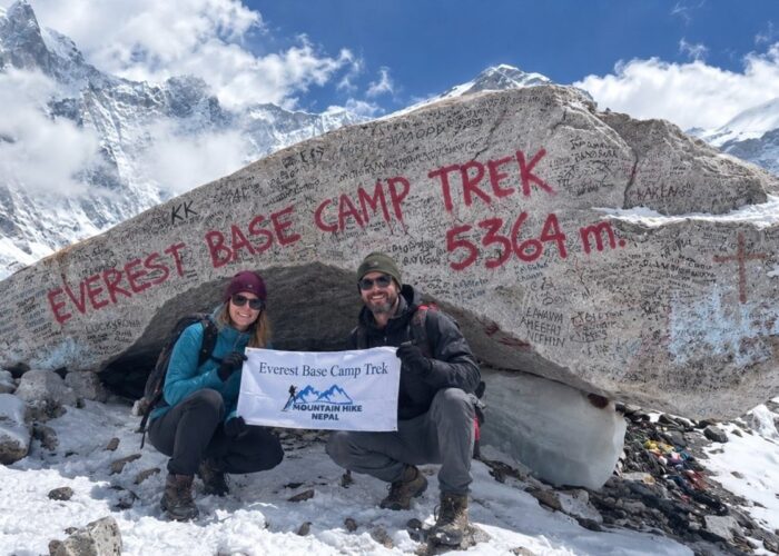 Two trekkers at Everest Base Camp with the 5,364-meter sign and snowy mountains