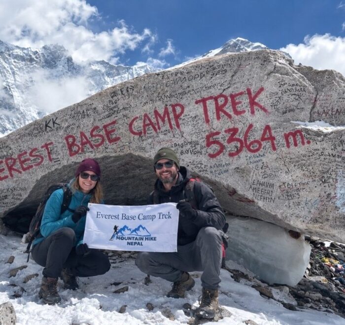 Two trekkers at Everest Base Camp with the 5,364-meter sign and snowy mountains