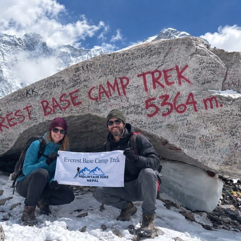 Two trekkers at Everest Base Camp with the 5,364-meter sign and snowy mountains