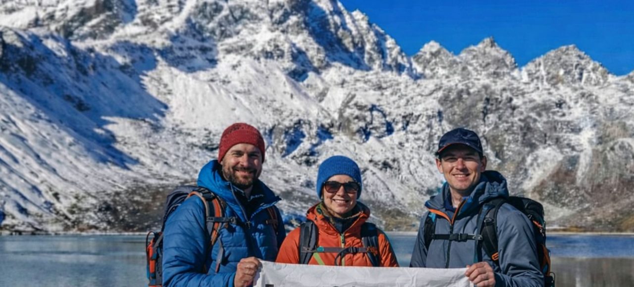 Trekkers at Gokyo Lake holding Everest Gokyo Lakes Trek banner with snow-covered Himalayan peaks