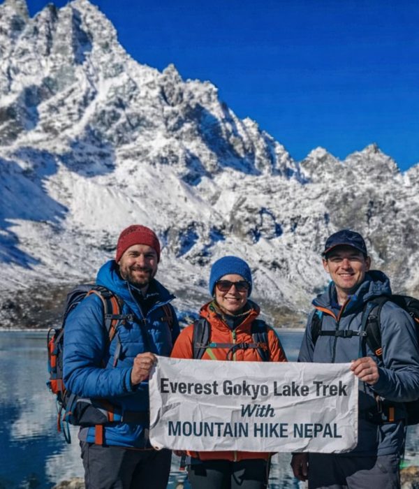 Trekkers at Gokyo Lake holding Everest Gokyo Lakes Trek banner with snow-covered Himalayan peaks