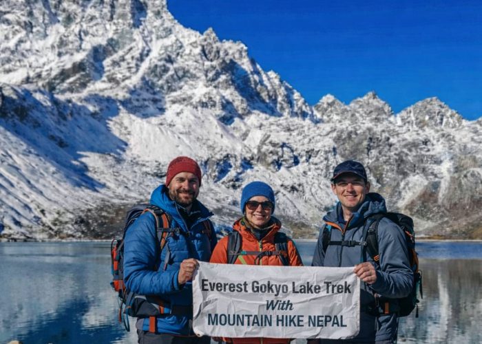 Trekkers at Gokyo Lake holding Everest Gokyo Lakes Trek banner with snow-covered Himalayan peaks
