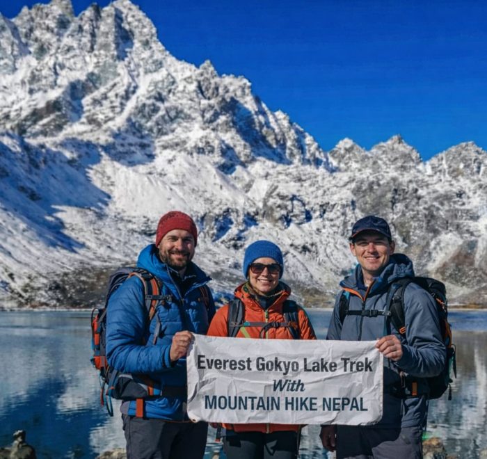 Trekkers at Gokyo Lake holding Everest Gokyo Lakes Trek banner with snow-covered Himalayan peaks