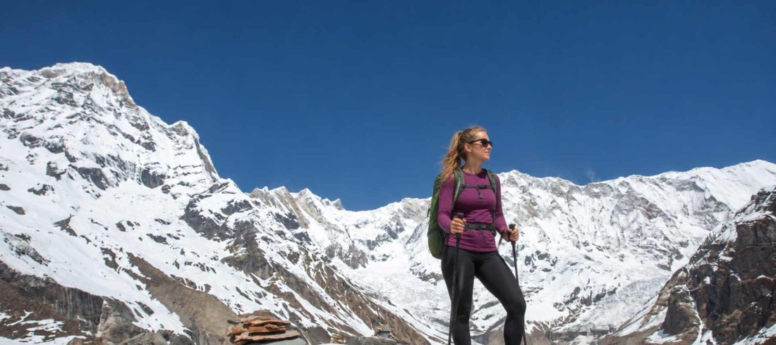 Annapurna Circuit trek for beginners with a female trekker standing on a mountain viewpoint overlooking the snow-covered Annapurna range in Nepal.