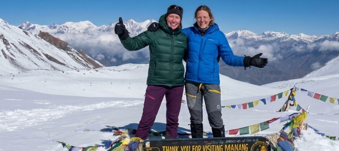 Trekkers standing at Thorong La Pass 5416m on the Annapurna Circuit in Nepal with snow-covered mountains and prayer flags