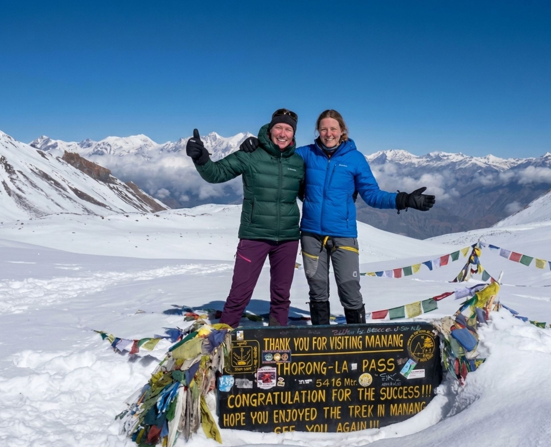 Trekkers standing at Thorong La Pass 5416m on the Annapurna Circuit in Nepal with snow-covered mountains and prayer flags
