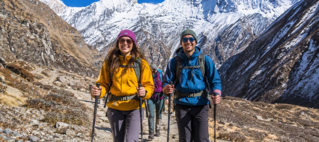 Beginner trekkers hiking on the Annapurna Base Camp trail surrounded by Himalayan mountains in Nepal.