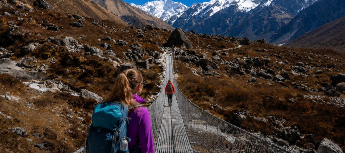 Female trekker crossing suspension bridge during the best time Langtang trek season with clear mountain views in Nepal