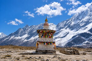Prayer-Flag Chorten on the Plateau Above Samagaon Whitewashed chorten wrapped in prayer flags on a rocky plateau, below steep snow-covered ridges