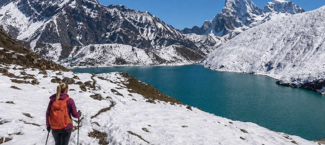 Trekker walking beside turquoise Gokyo Lake with snowy mountains during Gokyo Lakes Trek in Nepal