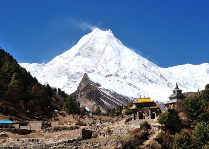 Mount Manaslu covered in snow, rising above a Buddhist gate and chorten on the Manaslu Circuit Trek
