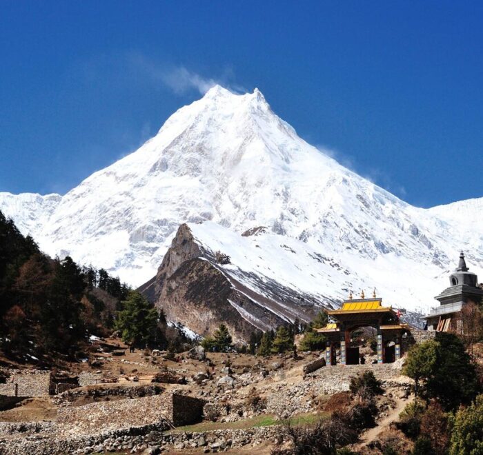 Mount Manaslu covered in snow, rising above a Buddhist gate and chorten on the Manaslu Circuit Trek