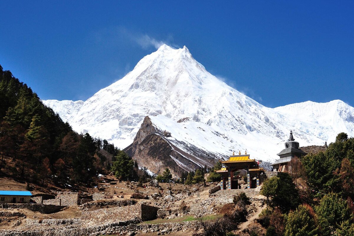 Mount Manaslu covered in snow, rising above a Buddhist gate and chorten on the Manaslu Circuit Trek