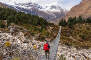 Suspension Bridge on the Manaslu Circuit Trek Trekker with a red backpack crossing a long suspension bridge over a rocky river on the Manaslu Circuit
