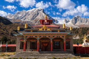 Monastery Prayer Hall in Samagaon, Manaslu Tsum Valley Trek Stone Buddhist prayer hall with painted woodwork and golden roof ornaments, with rocky snow peaks behind