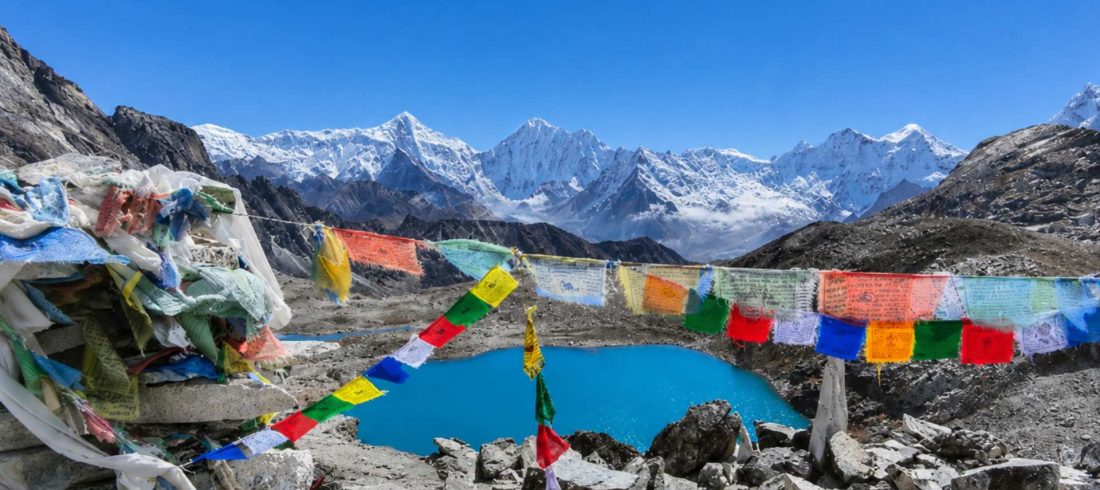Gokyo Lake surrounded by Himalayan peaks and prayer flags on the Everest Three Passes Trek in Nepal.