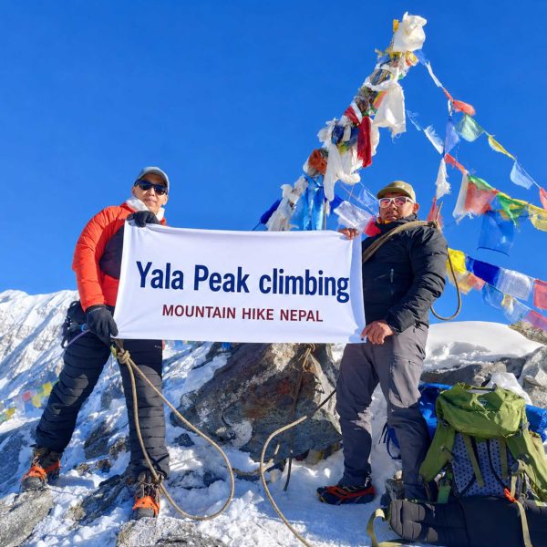 Climbers holding a Yala Peak Climbing banner at the 5,732m summit in Langtang Valley, Nepal with snow-covered Himalayan mountains and prayer flags in the background.