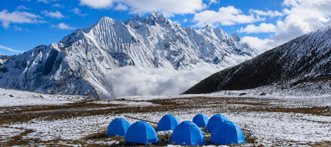 Blue expedition tents at Yala Peak High Camp in the Langtang Valley with snow-covered Himalayan mountains in the background.