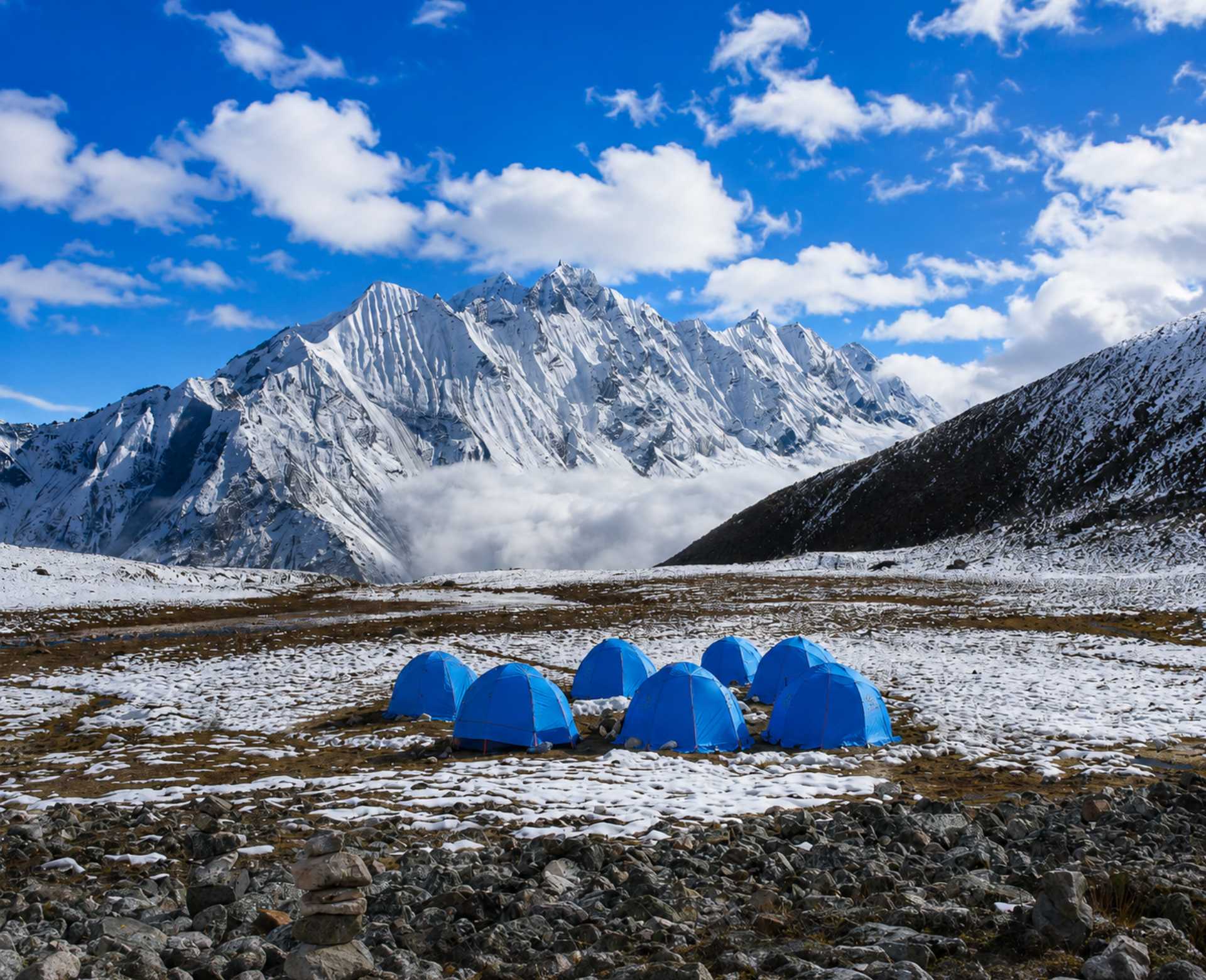 Blue expedition tents at Yala Peak High Camp in the Langtang Valley with snow-covered Himalayan mountains in the background.