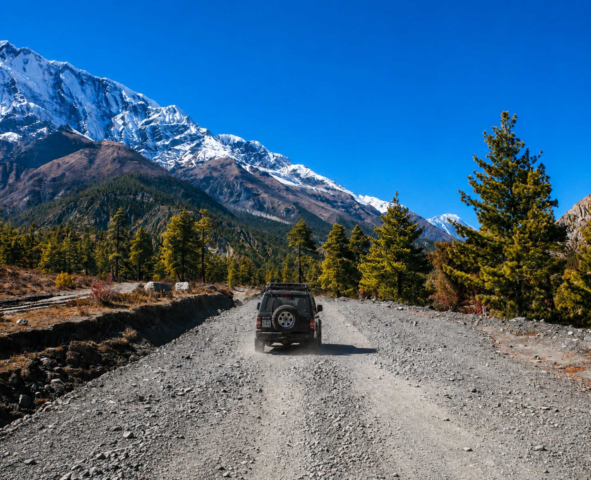 Manang Valley Jeep Tour – Scenic 4WD Adventure in Nepal Manang Valley Jeep Tour on a rugged 4WD road with snow-capped Himalayan mountains in the Annapurna region of Nepal