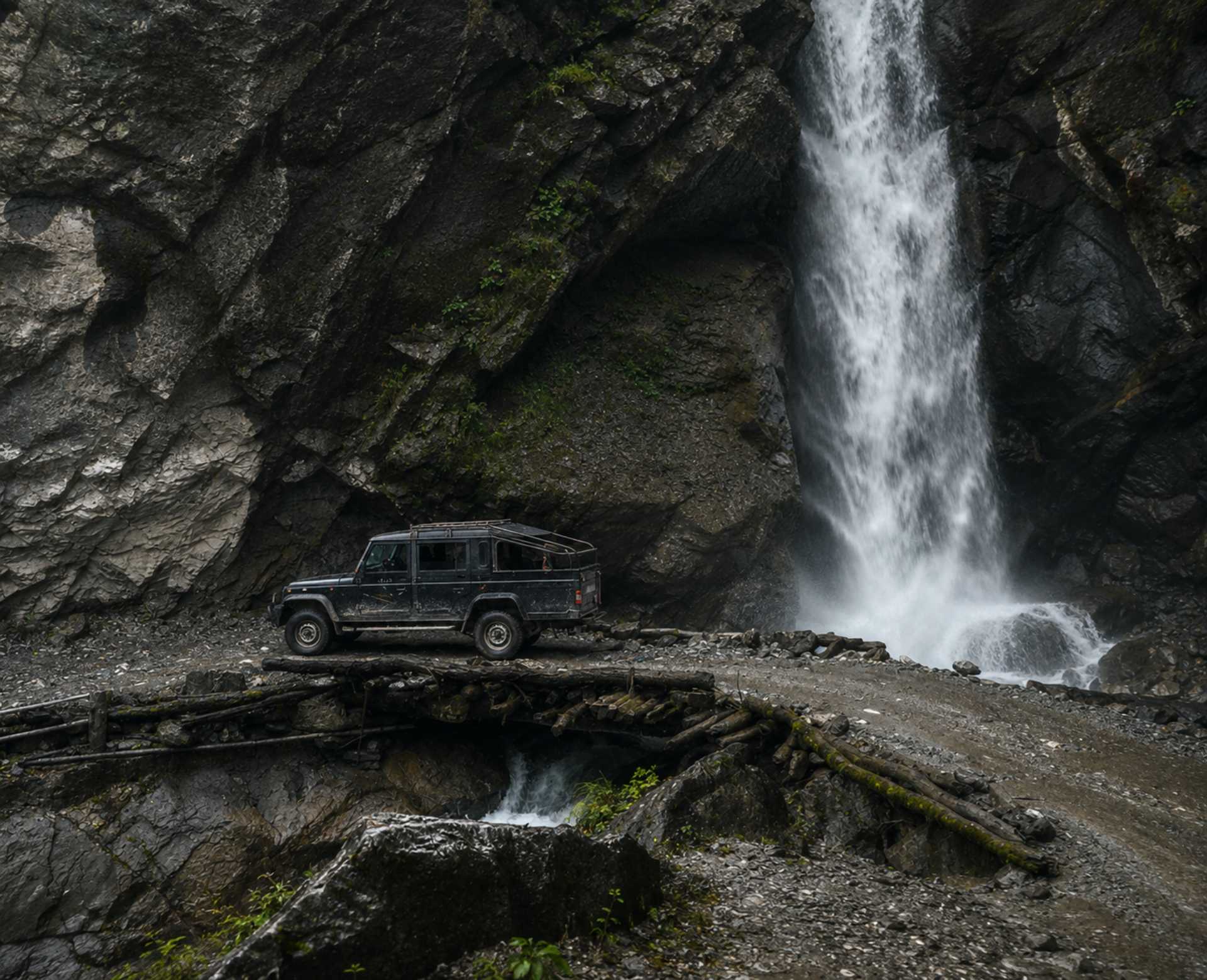 Manang Valley Jeep Tour – Waterfall Crossing by 4WD Jeep Black 4WD jeep crossing a wooden bridge beside a waterfall on the Manang Valley Jeep Tour in Nepal