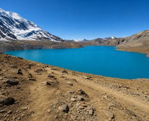 Turquoise Tilicho Lake with snow-covered peak and barren trail on the Annapurna Circuit