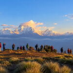 A group of trekkers gathered on the Poon Hill viewpoint ridge watching the golden morning sun light up the snow-capped Dhaulagiri peak in Nepal.