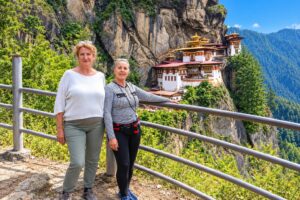 French Travelers at Tiger’s Nest – Bhutan Tour with Mountain Hike Nepal Two travelers at a viewpoint overlooking Paro Taktsang, Tiger's Nest in Bhutan.