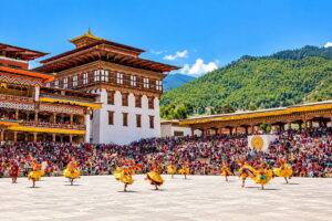 Thimphu Tshechu at Tashichho Dzong, Bhutan Dancers in traditional yellow silk costumes performing a Cham mask dance at the Thimphu Tshechu festival inside the courtyard of Tashichho Dzong in Bhutan.
