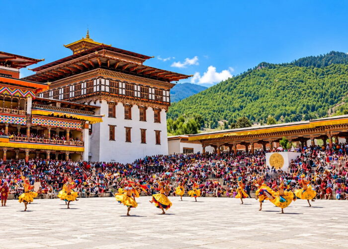 Dancers in traditional yellow silk costumes performing a Cham mask dance at the Thimphu Tshechu festival inside the courtyard of Tashichho Dzong in Bhutan.