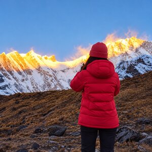 Trekker in a red down jacket watching sunrise light up the snow-covered Annapurna peaks