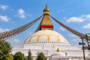 Boudhanath Stupa in Kathmandu, with its white dome, painted Buddha eyes and prayer flags against a blue sky