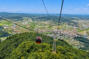 Chandragiri Cable Car A red cable car cabin rising over a forested hill above the valley floor