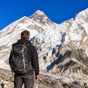 Trekker with a backpack facing a snow-covered peak above the rocky moraine on the Everest Base Camp trek
