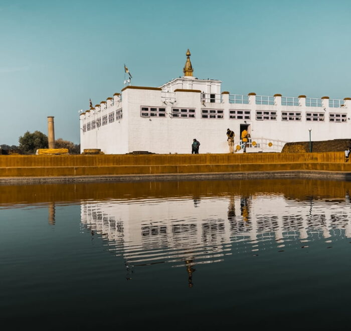 The white Maya Devi Temple in Lumbini reflected in the sacred pond, with the Ashoka Pillar on the left